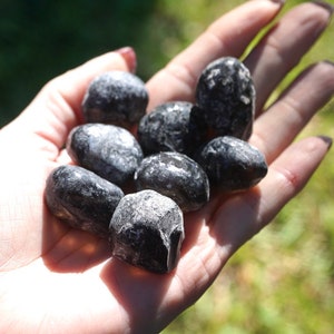 May include: A collection of black obsidian tumbled stones, smooth and polished, in a hand.