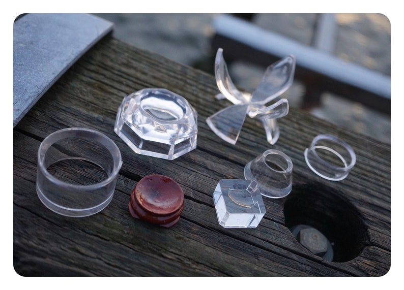 May include: A set of clear acrylic display stands for showcasing small objects. The set includes a variety of shapes and sizes, including a round ring, a square base, a cone, and a star-shaped stand. There is also a small wooden stand.