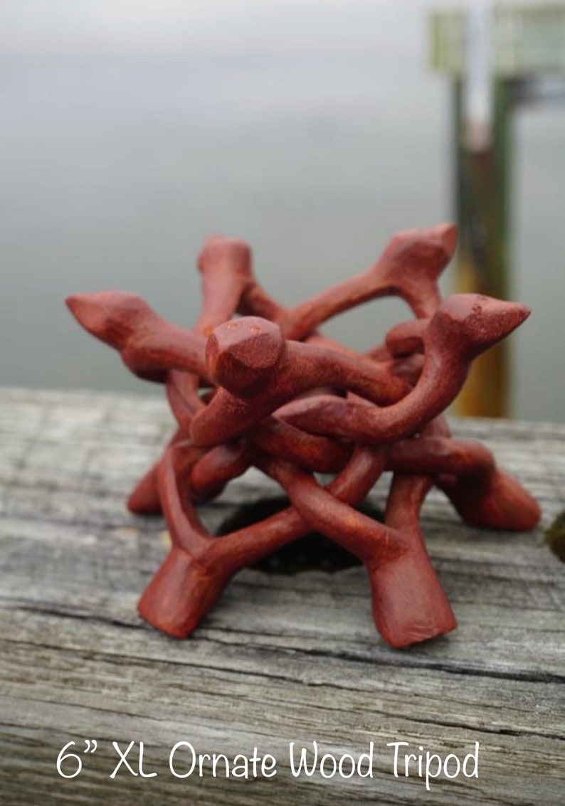 May include: A 6 inch extra large ornate wooden tripod stand, made of intricately carved wood, with a reddish-brown color.