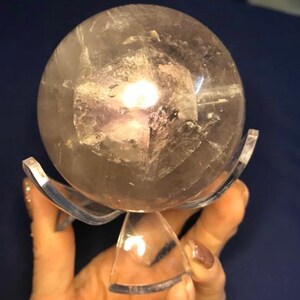 May include: A clear quartz crystal sphere with a cloudy, gray interior, resting on a clear acrylic stand.