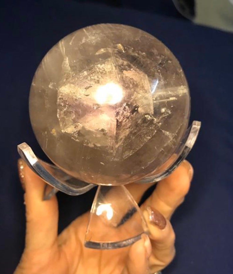 May include: A clear quartz crystal sphere with a cloudy, gray interior, resting on a clear acrylic stand.
