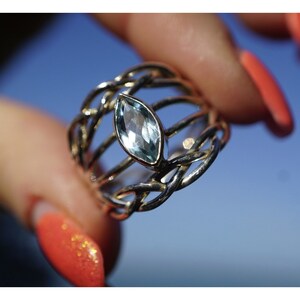 May include: A silver ring with a light blue gemstone set in a woven band.