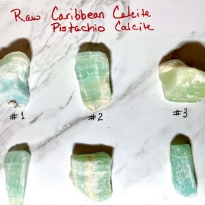 K&ouml;nnte beinhalten: Sechs rohe Pistazien-Calcit-Kristalle, nummeriert von 1 bis 3. Die Kristalle sind hellgr&uuml;n mit wei&szlig;en Adern.
