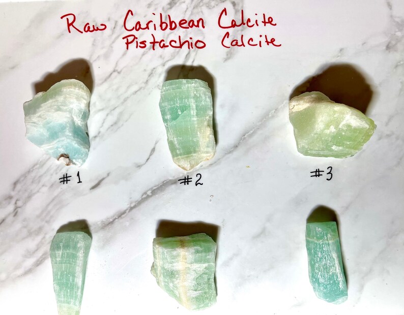 K&ouml;nnte beinhalten: Sechs rohe Pistazien-Calcit-Kristalle, nummeriert von 1 bis 3. Die Kristalle sind hellgr&uuml;n mit wei&szlig;en Adern.