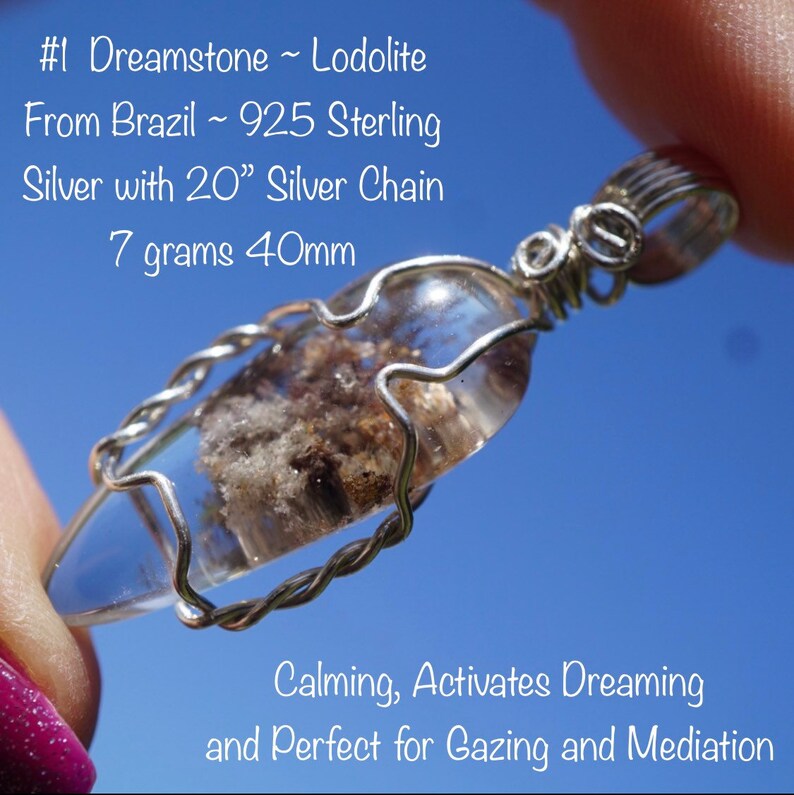May include: A clear quartz crystal pendant with a silver wire wrap, featuring a cloudy, gray inclusion. The pendant is attached to a silver chain. The pendant is 40mm in size and weighs 7 grams. The text "#1 Dreamstone ~ Lodolite From Brazil ~ 925 Sterling Silver with 20" Silver Chain 7 grams 40mm Calming, Activates Dreaming and Perfect for Gazing and Meditation" is visible in the image.