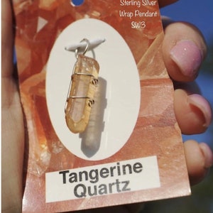 May include: A sterling silver wrap pendant featuring a tangerine quartz crystal. The pendant is wrapped in silver wire and has a loop for attaching a chain. The tag reads "Sterling Silver Wrap Pendant SW3 Tangerine Quartz".