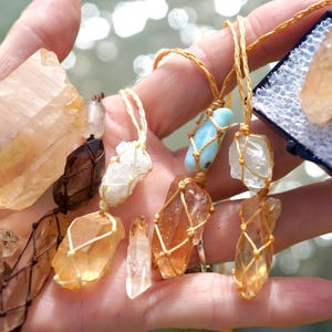 May include: A collection of crystal necklaces featuring various stones, including clear quartz, citrine, and a blue stone. The necklaces are crafted with macrame cord and showcase different knotting styles.
