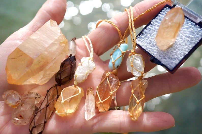 May include: A collection of crystal necklaces featuring various stones, including clear quartz, citrine, and a blue stone. The necklaces are crafted with macrame cord and showcase different knotting styles.