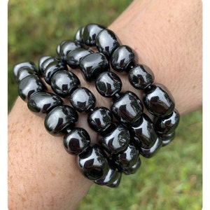 Puede incluir: Cuatro pulseras de cuentas negras apiladas en la mu&ntilde;eca de una persona. Las cuentas son redondas y tienen un acabado brillante y pulido.