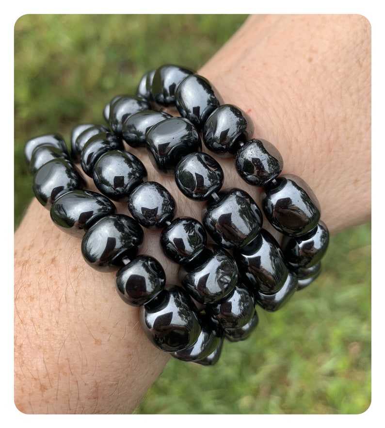 Puede incluir: Cuatro pulseras de cuentas negras apiladas en la mu&ntilde;eca de una persona. Las cuentas son redondas y tienen un acabado brillante y pulido.