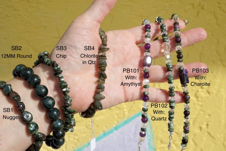K&ouml;nnte beinhalten: Eine Auswahl an Edelsteinarmb&auml;ndern mit runden, Chip- und Nugget-Designs, mit Amethyst-, Quarz- und Charoit-Akzenten. Die Armb&auml;nder sind mit Texten wie "SB2 12MM Round" und "PB101 With: Amythyst" beschriftet.