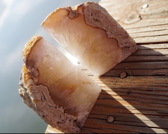 May include: Two halves of a large, light brown agate bookend with a white, translucent center. The agate is sitting on a wooden surface.