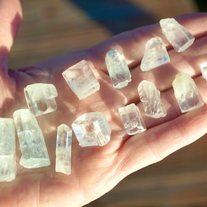Könnte beinhalten: Eine Sammlung von klaren, facettierten Aquamarin-Kristallen in verschiedenen Größen und Formen. Die Kristalle sind auf einer Hand angeordnet und zeigen ihre natürliche Schönheit und einzigartigen Formationen.