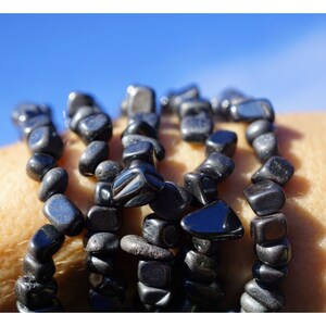 Puede incluir: Un conjunto de pulseras de piedras preciosas negras hechas con cuentas lisas de forma irregular. Las pulseras se llevan en la mu&ntilde;eca.
