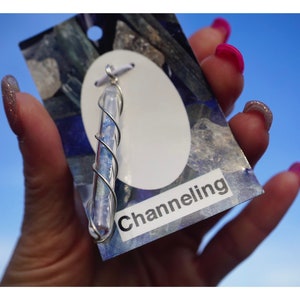 May include: A silver pendant featuring a clear glass tube filled with blue and white crystals. The pendant is labelled "Channeling".