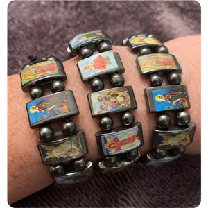 Puede incluir: Tres pulseras de cuentas negras con abalorios rectangulares de colores que representan im&aacute;genes religiosas. Los abalorios incluyen im&aacute;genes de santos, la Virgen Mar&iacute;a y Jes&uacute;s.