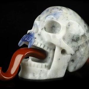 May include: A white crystal skull with a blue crystal tongue sticking out. The skull is carved with detail and has a red crystal tongue.