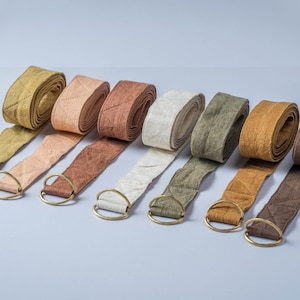 May include: A selection of yoga straps in shades like olive green, tan, and brown. Each strap is rolled up and has a gold-coloured metal ring. The straps feature a quilted diamond pattern.