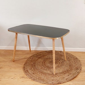 Può includere: Un tavolo nero con un bordo dorato e gambe in legno. Il tavolo è su un tappeto rotondo intrecciato.