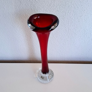 Peut inclure: Un vase en verre rouge avec un pied en verre transparent. Le pied a une surface textur&eacute;e avec de petites bulles. Le vase est haut et fin avec une large ouverture en haut.