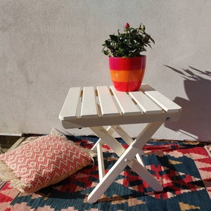 May include: A white folding table with a potted plant on top. The table is on a colorful rug with a red, white, and blue pattern. The plant is in a red, orange, and yellow pot.