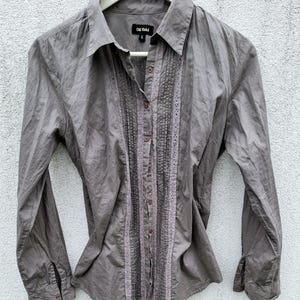 May include: A gray long-sleeved button-down shirt with a lace trim down the front. The shirt has a collar and a label that reads "Old  Riffel" with a size "L" on it.