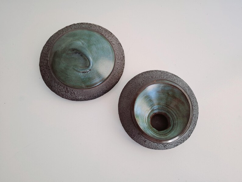 May include: Two ceramic bowls with a textured, dark gray rim and a teal interior. One bowl has a raised, curved design, while the other has a conical shape. The bowls are displayed against a white background.