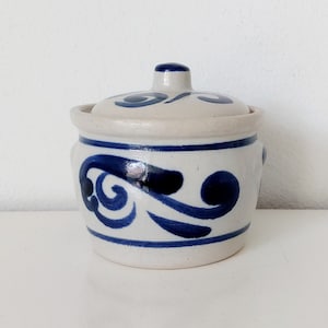 May include: A white ceramic jar with a lid, decorated with a blue and white swirl design. The jar has a rounded body and a slightly flared rim.