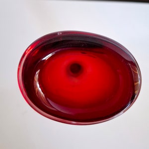 Peut inclure: Un vase en verre rouge fonc&eacute; avec un dessus rond en forme de bol. Le vase a une finition lisse et brillante.
