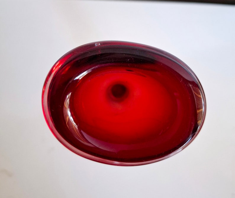 Peut inclure: Un vase en verre rouge fonc&eacute; avec un dessus rond en forme de bol. Le vase a une finition lisse et brillante.