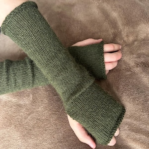 Può includere: Un paio di guanti senza dita di lana verde con un polsino lungo. I guanti sono fatti di un filato morbido e soffice.