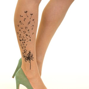 May include: A pair of nude sheer tights with a black dandelion design featuring musical notes. The dandelion is on the lower leg and the notes are blowing in the wind.