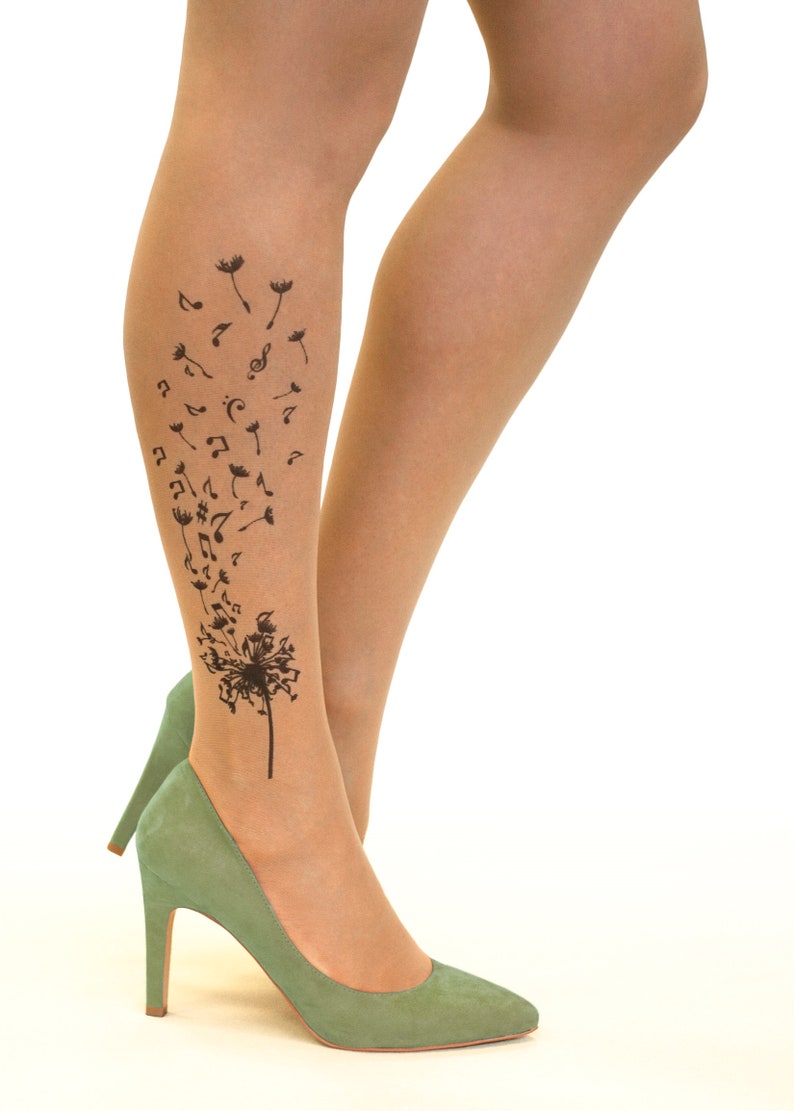 May include: A pair of nude sheer tights with a black dandelion design featuring musical notes. The dandelion is on the lower leg and the notes are blowing in the wind.