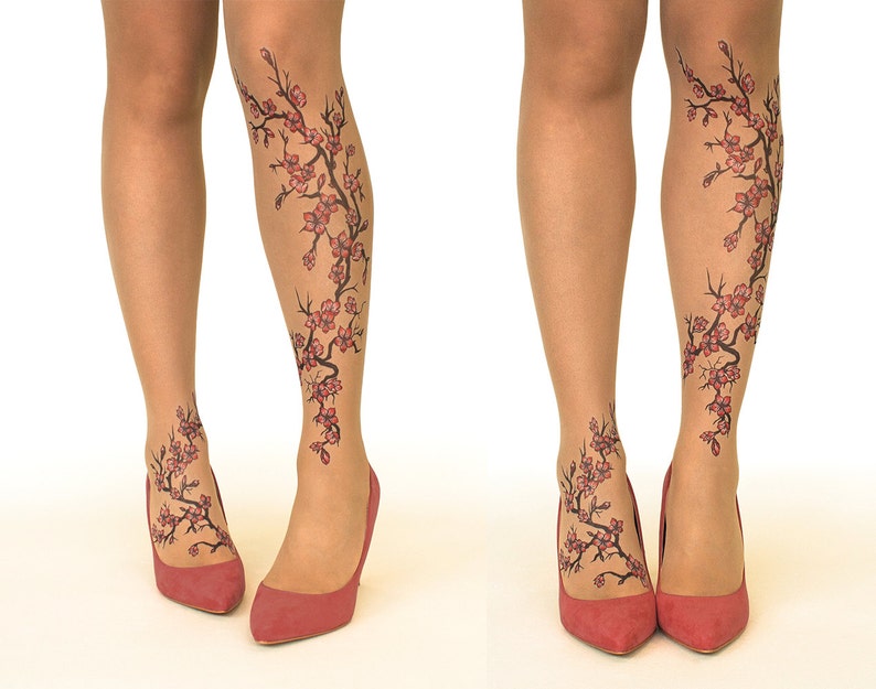 Puede incluir: Un par de medias transparentes con un dise&ntilde;o floral impreso en las piernas. El dise&ntilde;o presenta una rama de cerezos en flor con flores rosas y tallos negros. Las medias se muestran en una modelo que lleva tacones rojos.