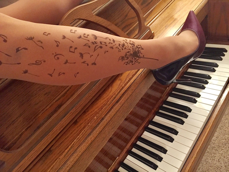 May include: A woman's leg with a tattoo of musical notes and a dandelion on it. She is wearing a pair of dark purple high heels and is sitting at a piano.