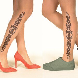 Op de afbeelding: Een paar transparante panty's met een zwart Keltisch knoopontwerp dat langs de achterkant van elk been loopt. Eén been is gecombineerd met koraalkleurige hoge hakken, het andere met olijfgroene sneakers.