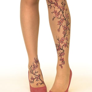 Puede incluir: Un par de medias transparentes con un dise&ntilde;o floral en las piernas. El dise&ntilde;o presenta una rama negra con flores rojas, que se asemeja a un &aacute;rbol de cerezo en flor.