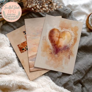 a close-up of a collection of artworks or cards, including a heart-shaped card with a cross and lace-like details, all resting on a soft, textured surface.