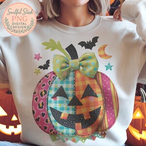Puede incluir: Una sudadera blanca con un diseño de calabaza de retazos sonriente. La calabaza tiene un lazo de lunares verdes y amarillos, y está rodeada de murciélagos, estrellas y una luna creciente. El texto "Soulful Stash PNG DIGITAL DESIGN" está en la esquina superior izquierda.