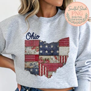 May include: A light gray sweatshirt featuring a patchwork design of the state of Ohio. The Ohio outline is filled with a mix of floral, plaid, and star-spangled patterns in red, white, and blue. The word "Ohio" is written in cursive.