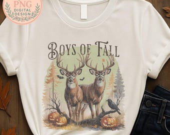 May include: Cream-colored t-shirt featuring a fall-themed graphic. The design includes two deer with large antlers, pumpkins, bats, and the text "BOYS OF FALL". The artwork has a vintage, distressed look.