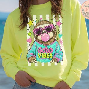 A person wearing a yellow sweatshirt with a graphic of a sloth wearing sunglasses and the text "GOOD VIBES" printed on it.