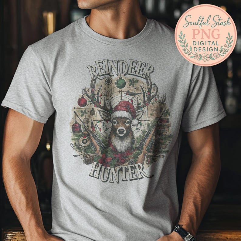 May include: A light gray t-shirt featuring a detailed graphic of a reindeer wearing a Santa hat, antlers, and holding rifles. The text "REINDEER HUNTER" is arched above and below the reindeer image. A digital design logo is in the upper right corner.