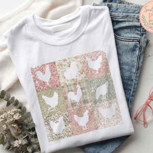 Op de afbeelding: Wit T-shirt met een patchwork ontwerp van witte kippensilhouetten op bloemen- en ruitpatronen. Het shirt heeft de tekst "Soulful Stash PNG Digital Design" in een cirkelvormig logo. Het shirt wordt getoond met een blauwe jeans en een roze bril.
