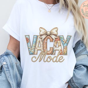 Puede incluir: Camiseta blanca con las palabras "VACAY Mode" en una fuente decorativa, adornada con un lazo y elementos marinos. Las letras son en tonos azules, beige y coral, evocando un tema de playa. La camiseta se lleva con una chaqueta vaquera.