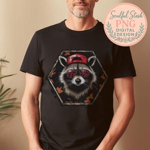 Könnte beinhalten: Schwarzes T-Shirt mit einem Waschbären-Design. Der Waschbär trägt eine rote Kappe und Sonnenbrille mit dem Text "RAD DAD". Das Design befindet sich in einem Sechseck mit Camouflage-Muster. Ein "Soulful Stash PNG DIGITAL DESIGN"-Logo ist sichtbar.