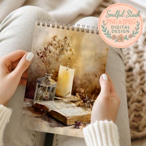 A person's hands holding a spiral-bound notebook with a watercolor painting of a vase with flowers and a candle on an open book.