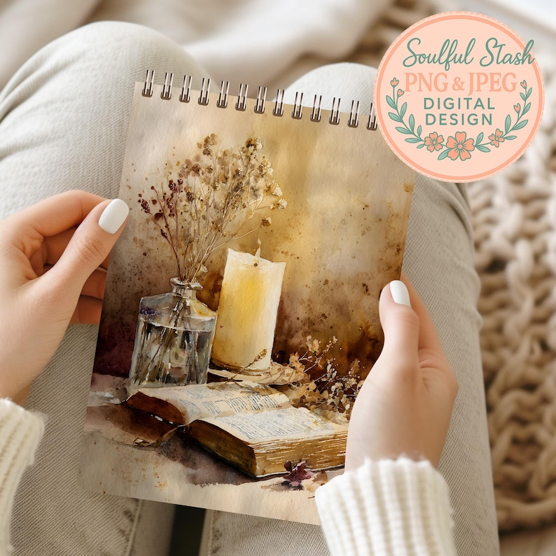 A person's hands holding a spiral-bound notebook with a watercolor painting of a vase with flowers and a candle on an open book.