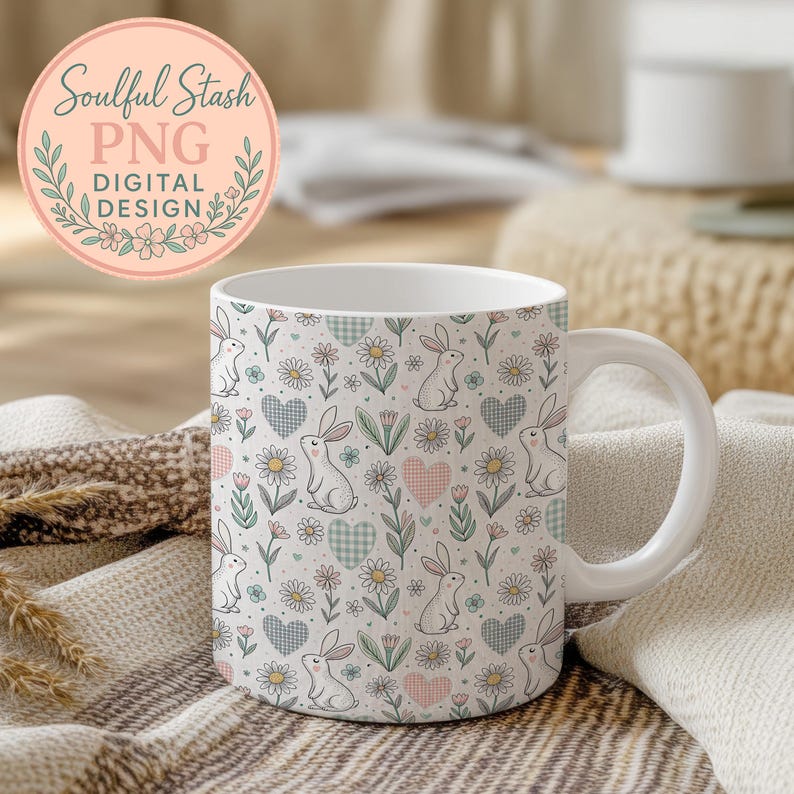 A white mug with a floral pattern featuring rabbits, hearts, and flowers is placed on a beige blanket.