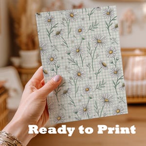 A hand holding a card with a floral pattern on it, in a room with a crib and other furniture.